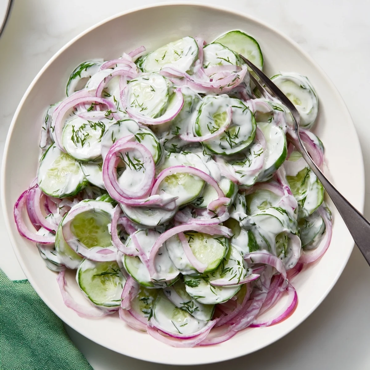 Close-up of Creamy German Cucumber Salad, showcasing the fresh dill and red onion on top.