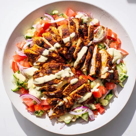 A colorful close-up shows tender chicken shawarma nestled on a vibrant salad, drizzled with tahini.