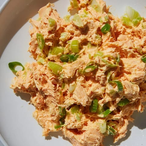 A close-up of zesty tuna salad glistening with lemon juice, garnished with parsley and lemon wedges on a rustic board.